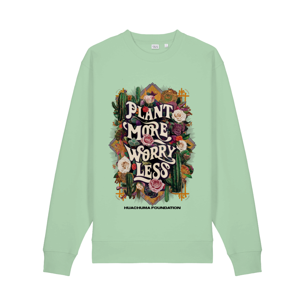 A pale green sweatshirt printed Plant More Worry Less in painted lettering among cacti and roses, with Huachuma Foundation beneath