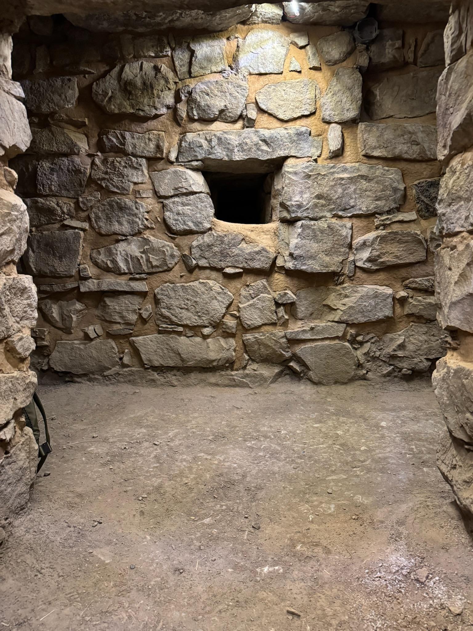 A small stone chamber in the galleries at Chavín de Huántar, a square opening set into the masonry wall above a bare earth floor